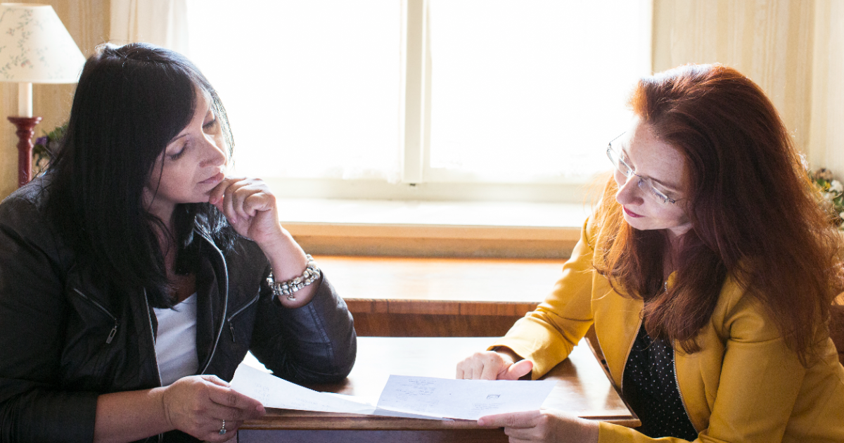 Zwei Frauen sitzen sich an einem Tisch gegenüber und besprechen gemeinsam Unterlagen in ruhiger, konzentrierter Atmosphäre.